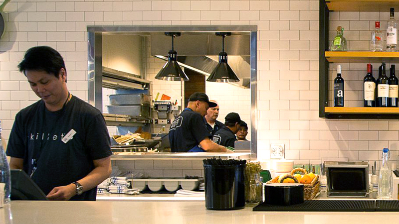 A vendor at SEA Airport behind the counter prepares food for passengers.