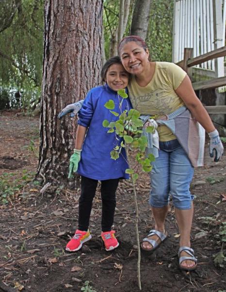 Woman and young girl stand next to a tree that they have just planted